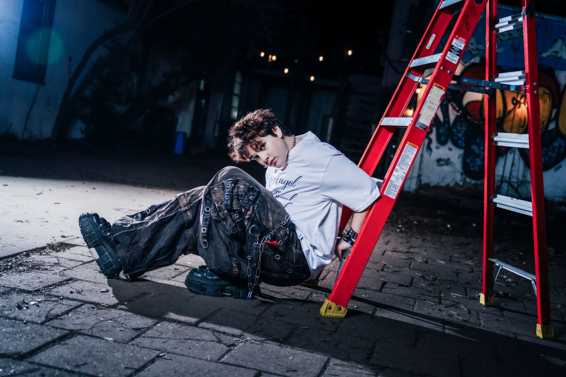 Modest Angel campaign, model seated beside a red ladder at night